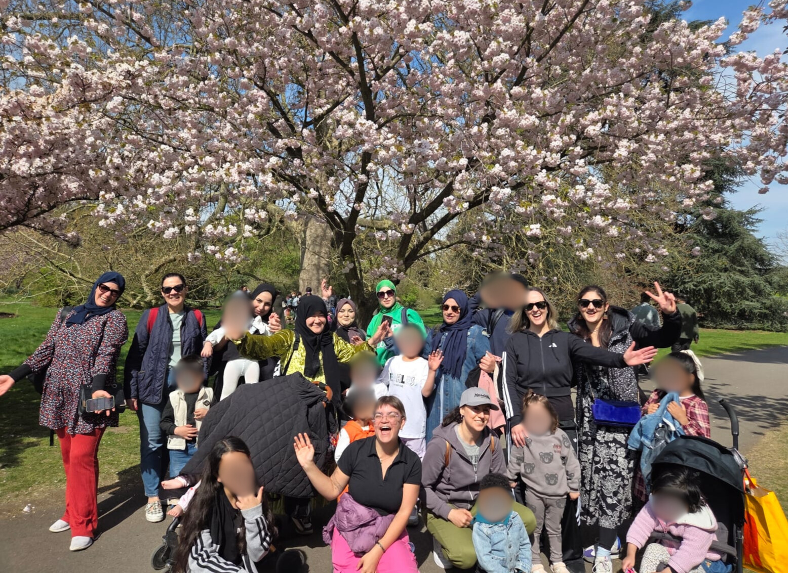Group faces blurred Kew April2025 Group of women and children under tree heavy with blossom
